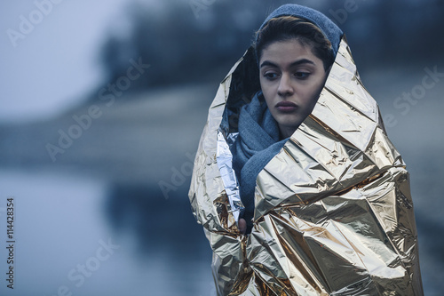 Thoughtful teenage girl wrapped in golden plastic at lakeshore during winter