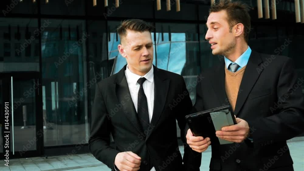 Slow motion: Two white young managers with tabletpc internet serfing. Glass business centre at the BG. teal and orange style. Slow motion: Two white young managers with tabletpc internet serfing. Glass business centre at the BG. teal and orange style.