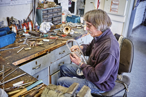 Instrument maker repairing trumpet in workshop photo