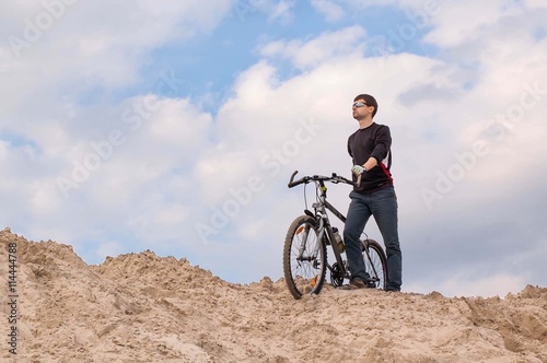 Cyclist stands on the sand against the sky