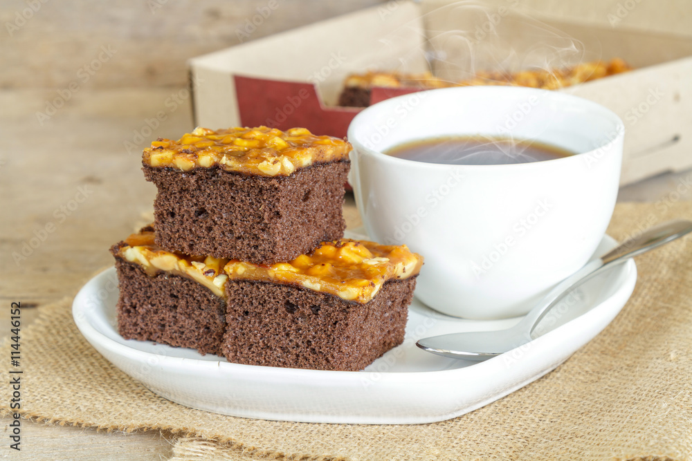 Toffee cake garnish with cashew and hot coffee on wooden table.