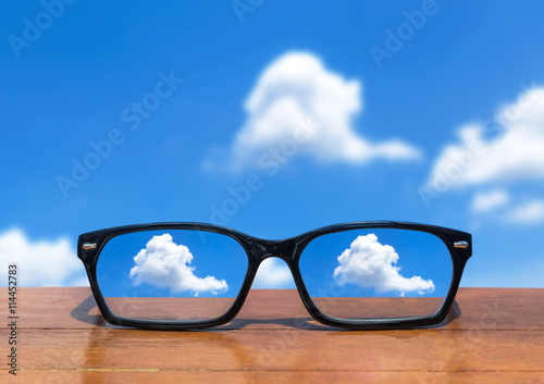 eyeglasses on wooden table front of abstract white clouds on deep blue sky background