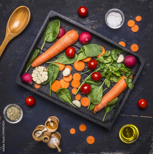 Delicious assortment of farm fresh vegetables sliced carrots, fresh spinach leaves, seasonings and butter, cherry tomatoes laid out in a wooden box, spread around spices and herbs