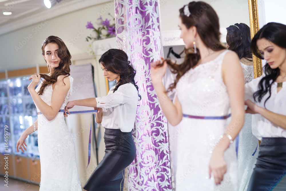 Female trying on wedding dress in a shop with women assistant.