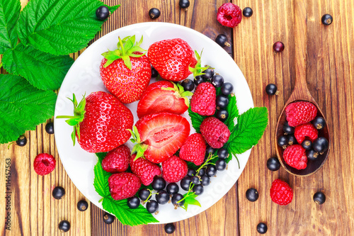 Mix of fresh  ripe berries in plate and spoon on wooden background  top view.