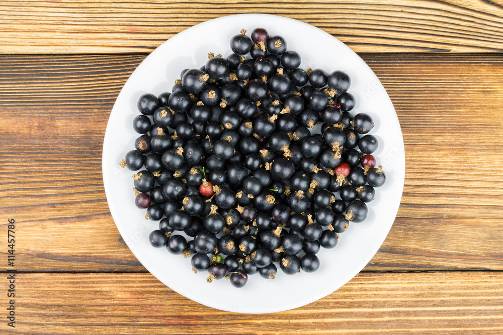 Black ripe currant in plate on wooden background, top view Black ripe currant in plate on wooden background, top view