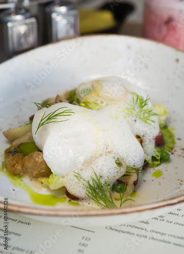 Beautiful fresh white steamed cod fillet, served with a white creamy sauce, shallots, peas and seasoning in a rustic dish.