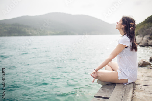 Yoga and meditation concept.Woman meditating in sitting yoga position on pier.Woman alone practicing mindfulness meditation to clear her mind.Zen,meditation,peace concept