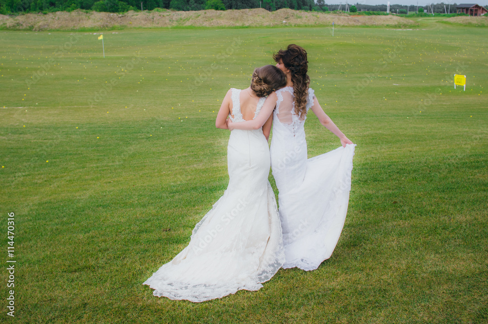 Two beautiful brides embracing on the green field of the golf club Two beautiful brides embracing on the green field of the golf club
