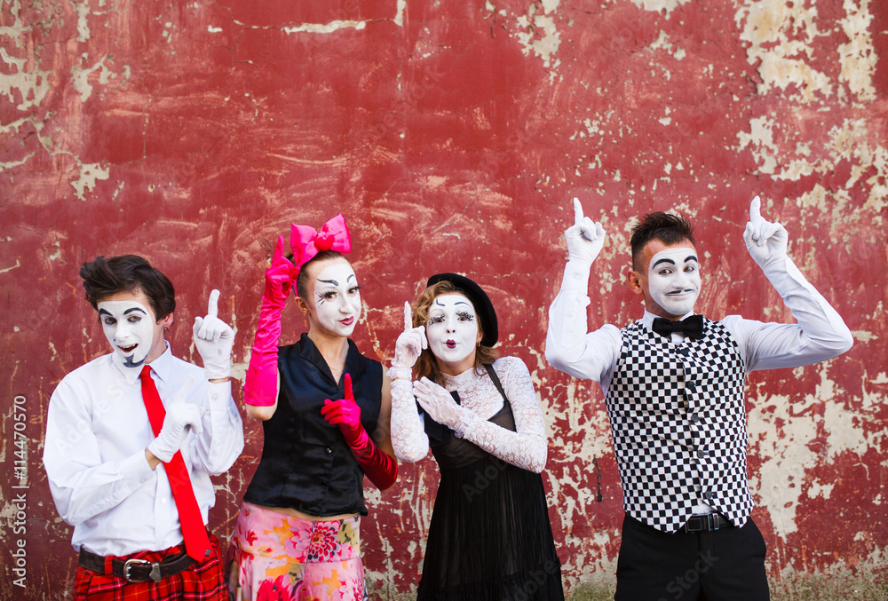 Obraz premium Four mimes point to the top on a red wall.