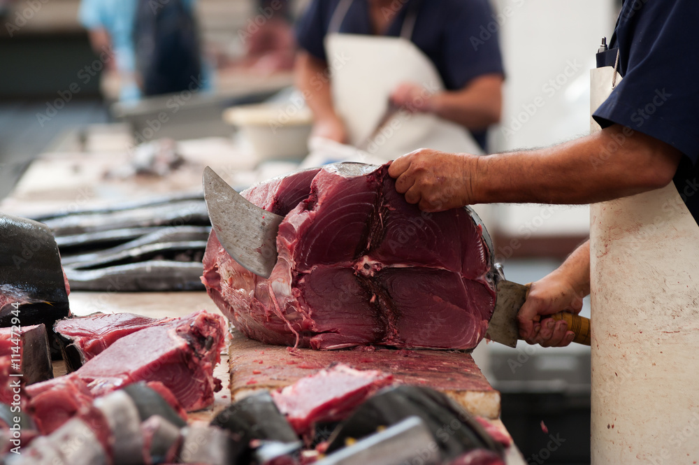 Fisherman (salesman) is cutting fresh tuna fish in the open air fish market or restaurant. Mercado dos Lavradores, Funchal, Madeira island, Portugal.