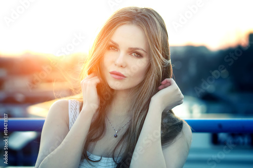 Outdoor portrait of young pretty sexy woman with sensual lips posing at roof at the end of bright sunset. Lovely soft back light.