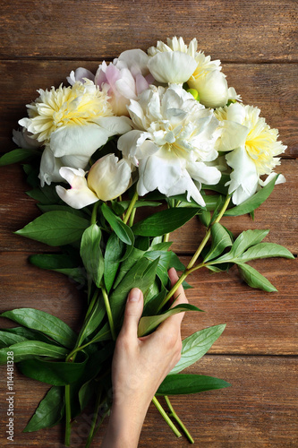 Female hand holding beautiful white peony flowers on wooden background
