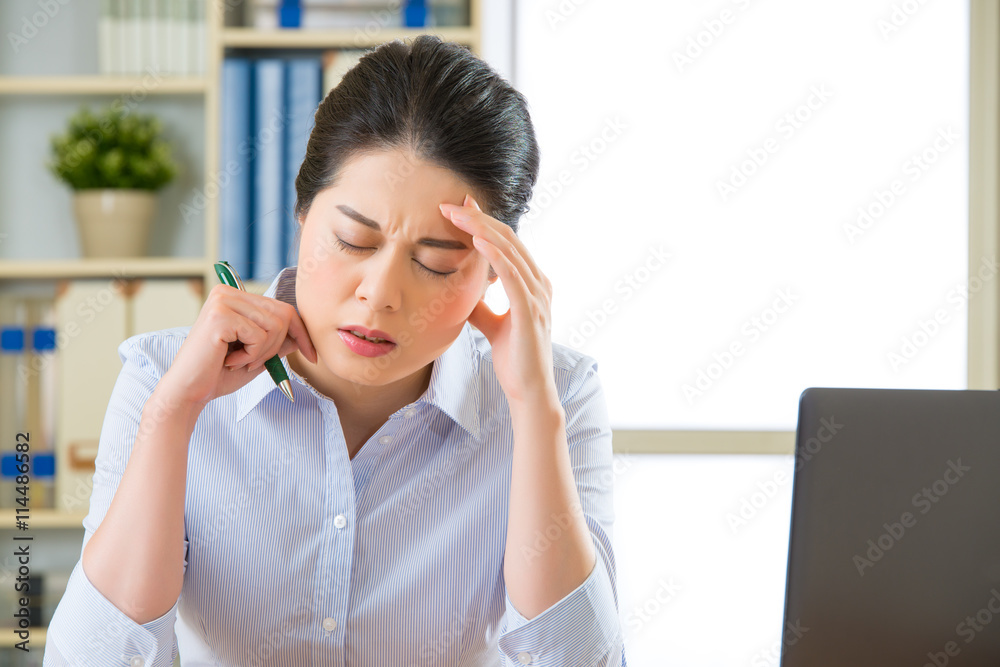 Young asian business woman writing with headache Young asian business woman writing with headache