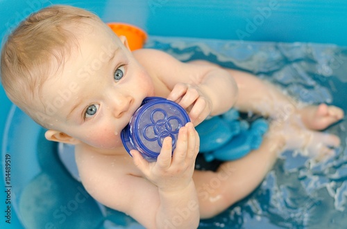 Cute baby bathing in a tube and playing with plastic caps. He is looking at his parents. photo