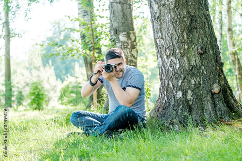 Portrait of young hipster man with camera outdoors. Young male photographer photographing nature on summer day. © Iurii