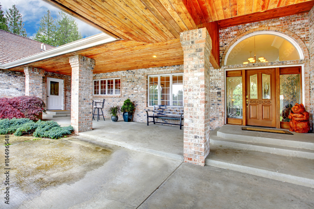 Cozy entrance porch of a large brick house. Patio area with concrete floor and brick columns.