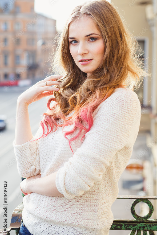 Portrait of young lady wearing white pullover posing on a balcony
