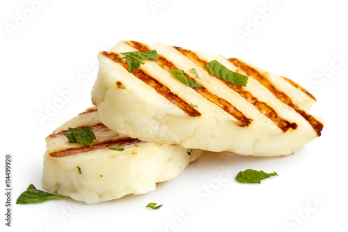 Two grilled slices of halloumi cheese isolated on white in perspective. With grill marks and mint.