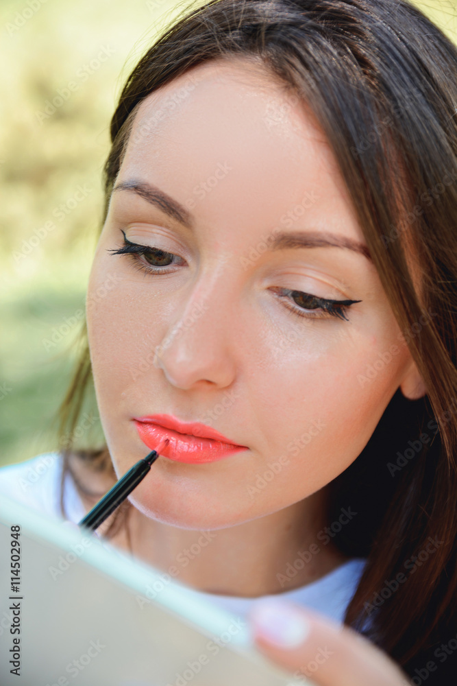 Woman making Make-up at park. Lipgloss. Lipstick Woman making Make-up at park. Lipgloss. Lipstick