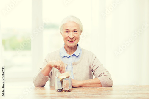 senior woman putting money into glass jar at home