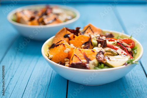 Healthy Paleo Salad with Pumpkin, Sweet Potato, Red Pepper and Nuts on Blue Wooden Background, Close-up