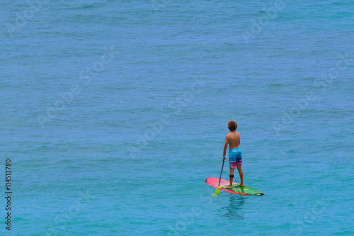 A Boy paddelboarding on a calm Pacific ocean morning