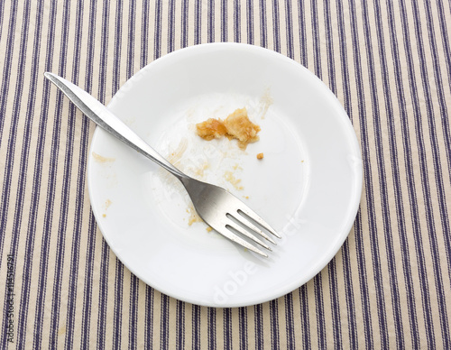 Finished apple pie on plate with a fork atop a blue striped tablecloth.