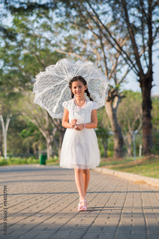 Lovely preteen girl with white lace umbrella walking in park