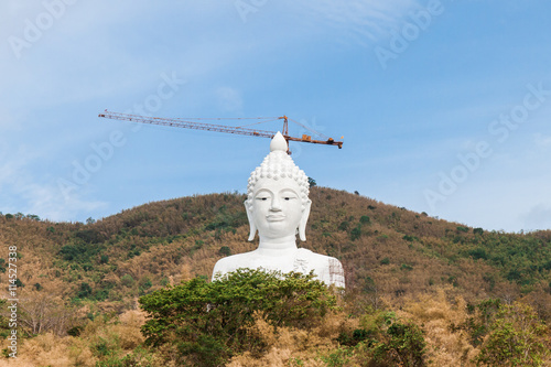 white buddha on  mountain with crane and scaffolding
