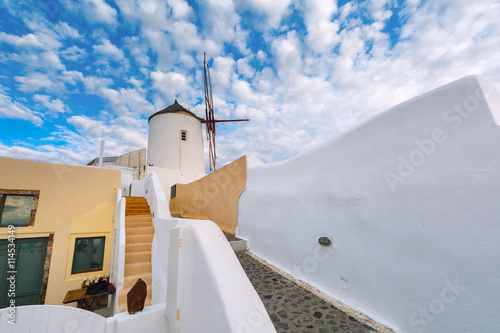 White windmill and picturesque cloudy sky in Oia or Ia on the island Santorini, Greece