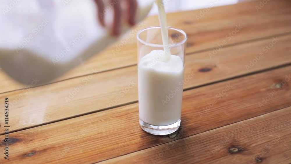 hand pouring milk into empty glass on wooden table hand pouring milk into empty glass on wooden table