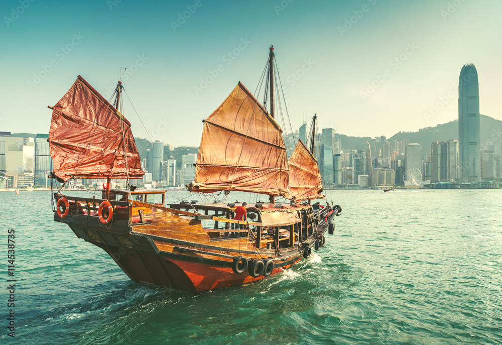 Obraz premium Scenic view over Hong-kong skyscprapers and a junkboat sailing. Iconic landmark of Hong-Kong.