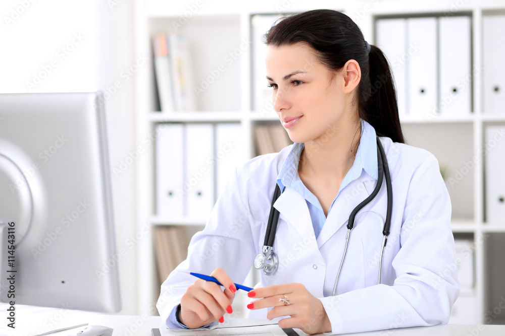 Young brunette female doctor sitting at the table and working by computer at hospital office. Doctor is in trouble with diagnosis. Health care, insurance and help concept. Young brunette female doctor sitting at the table and working by computer at hospital office. Doctor is in trouble with diagnosis. Health care, insurance and help concept.