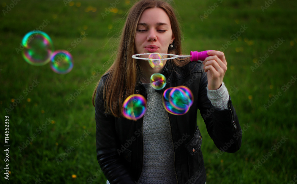 Soft and blur conception. Young beautiful girl blowing colorful bubbles outdoors