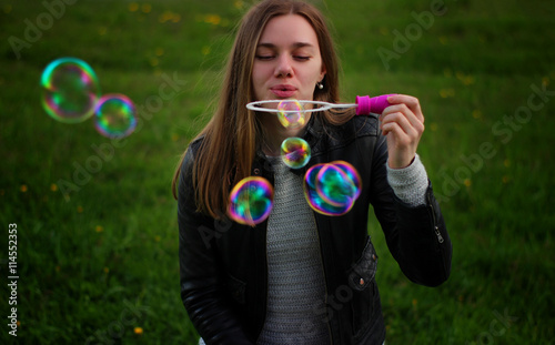 Soft and blur conception. Young beautiful girl blowing colorful bubbles outdoors