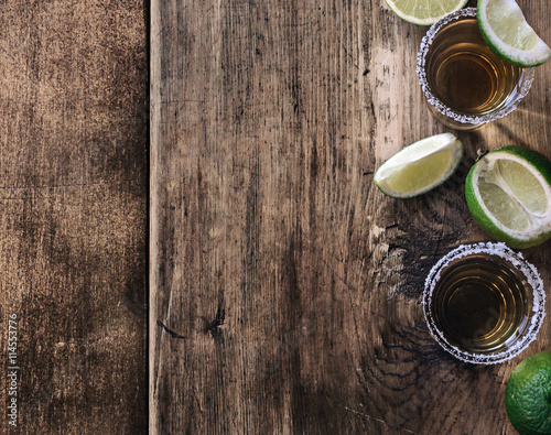 Tequila shots with lime slice on dark wooden board, top view