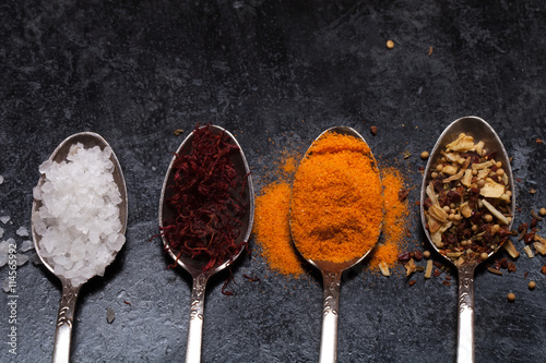 Old metal spoons with different kind of spices on a black backgr