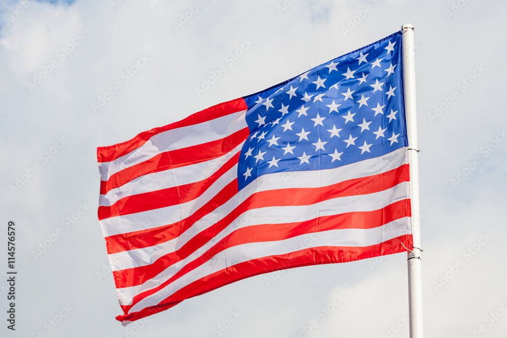Close-up American flag waving against cloudy blue sky background