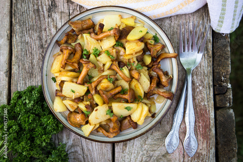 fried young potatoes with chanterelles mushrooms in bowl on old