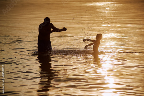 Father and son playing on the beach during sunset.