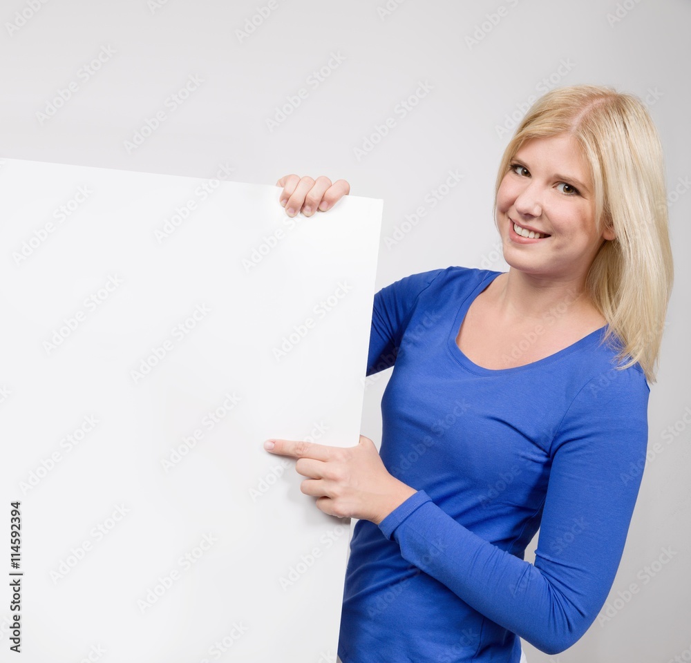 Junge blonde Frau zeigt auf leere Werbetafel zum Beschriften Junge blonde Frau zeigt auf leere Werbetafel zum Beschriften