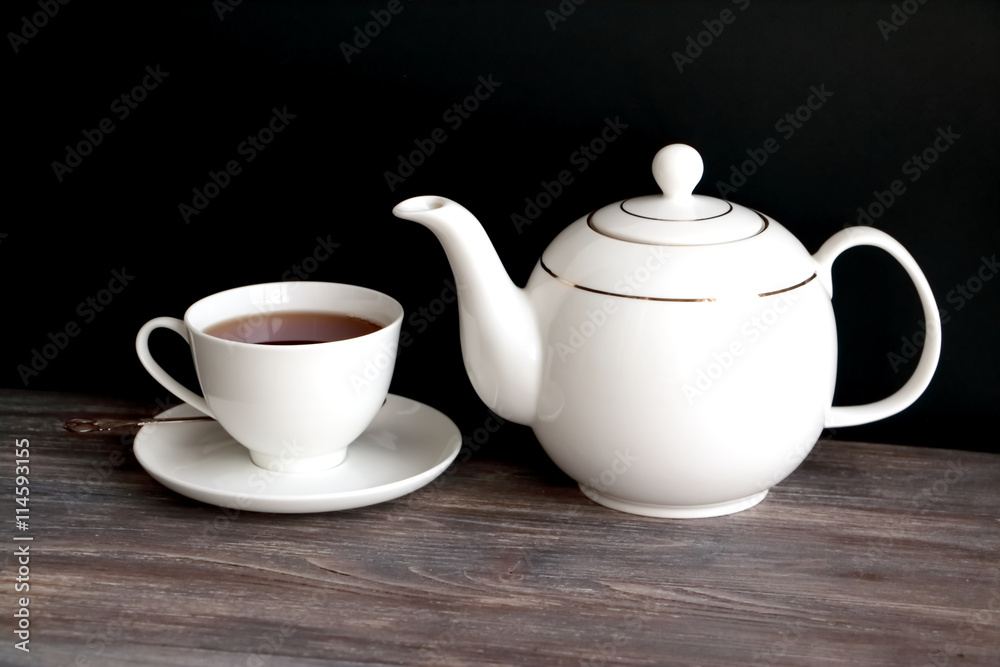 Tea pot, tea cup with black tea. Wooden table, black background. Chinese porcelain.