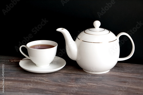 Tea pot, tea cup with black tea. Wooden table, black background. Chinese porcelain.