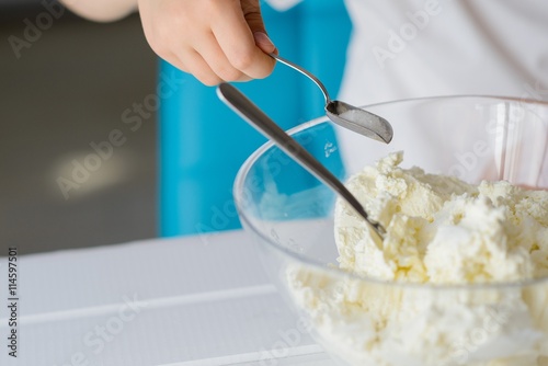 Child adding sugar to cottage cheese in a bowl.