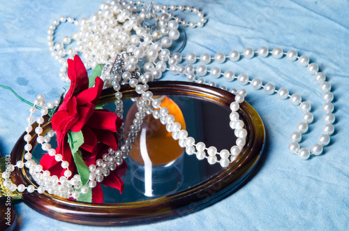 still life: pearl necklace, glass of white wine, mirror, flower on blue background photo