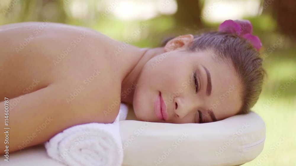 Pretty young woman having a spa treatment lying naked on a beauty couch outdoors in a tropical garden looking at the camera with a quiet smile. Pretty young woman having a spa treatment lying naked on a beauty couch outdoors in a tropical garden looking at the camera with a quiet smile.