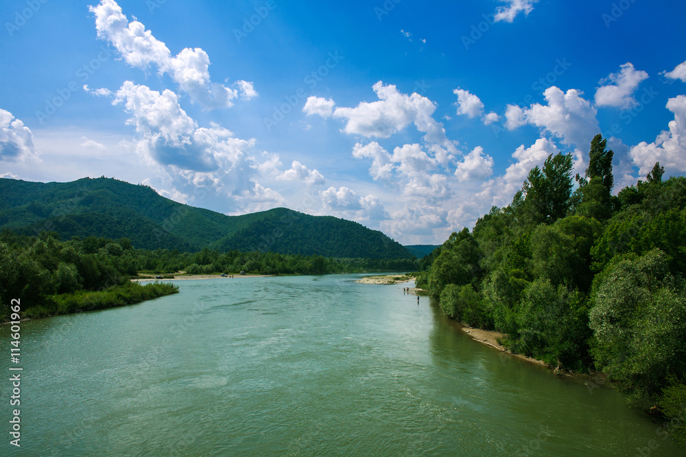 River in mountain valley in woods on blue sky background River in mountain valley in woods on blue sky background