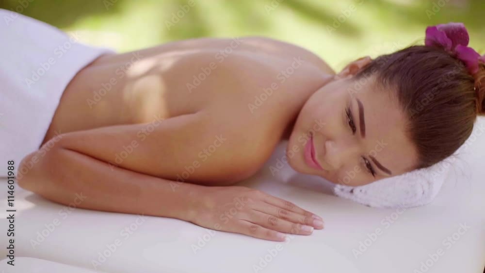 Smiling happy young woman having a spa treatment outdoors in a garden lying naked on a spa bed draped in a white towel smiling with pleasure. Smiling happy young woman having a spa treatment outdoors in a garden lying naked on a spa bed draped in a white towel smiling with pleasure.