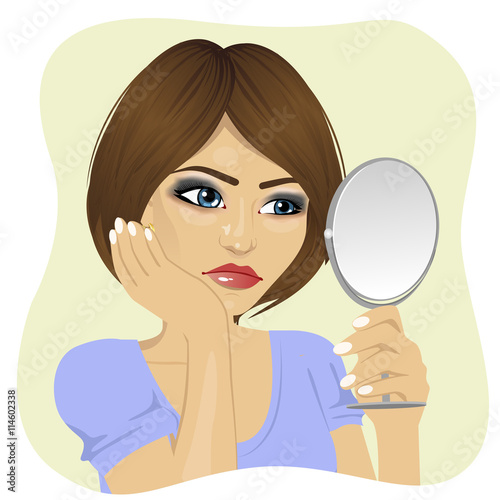 Concerned young woman looking at herself in mirror